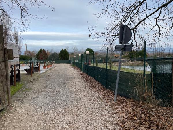 Chemin de gravier le long d'un filet vert séparant l'itinéraire d'un étang et, à gauche, des plantes d'un restaurant.